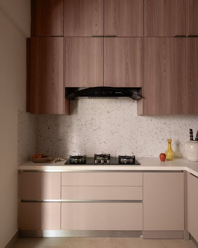 Modern kitchen with wood upper cabinets, terrazzo backsplash, black hob, and pink lower cabinetry