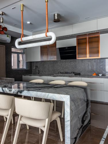 Kitchen island with veined marble waterfall countertop under a tube pendant light, ribbed cabinet fronts behind