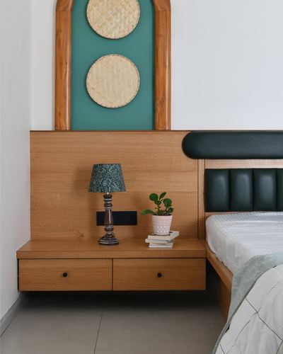 Floating wooden nightstand with lamp and plant beside dark tufted headboard, arched niche with cane discs above