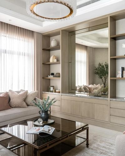 Pink and beige living room with wood shelving, mirror panel, and glass coffee table