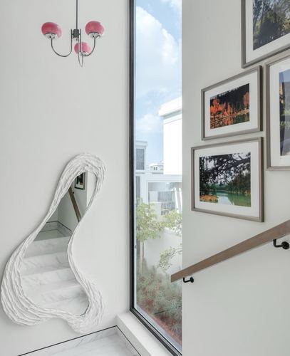 Sculptural white mirror beside a gallery wall and window overlooking a staircase and courtyard