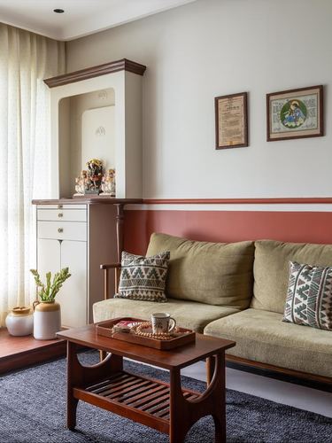 Living room corner with white pooja cabinet, terracotta dado wall, and olive sofa with embroidered cushions