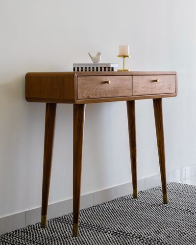 Wooden console table with two drawers, brass-tipped tapered legs, styled with books, a bird figurine and candle holder.
