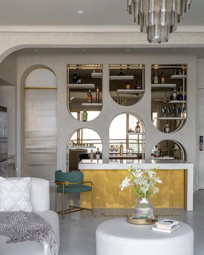 Home bar with arched mirrored niches, gold fluted front, marble counter, and teal velvet chair