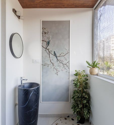 Bathroom corner with black marble pedestal sink, round mirror, and bird motif wall panel beside a window