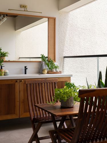 Wooden vanity with cane-framed mirror opens onto a balcony with folding wood chairs and plants