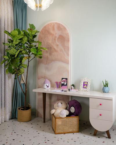 Child's study desk with pink drawers set into an arched stone niche beside a potted fig plant