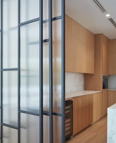 Fluted glass partition beside a wood-cabinet kitchen with marble-look backsplash and island