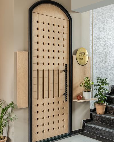 Arched black-framed wooden door with perforated circular pattern and chain handle, entry foyer with plants