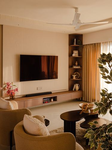 Warm-toned living room with wall-mounted tv, floating wood console, corner shelf, and boucle armchairs