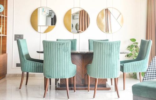 Dining room with six teal velvet chairs around a dark wood table beneath three round brass mirrors