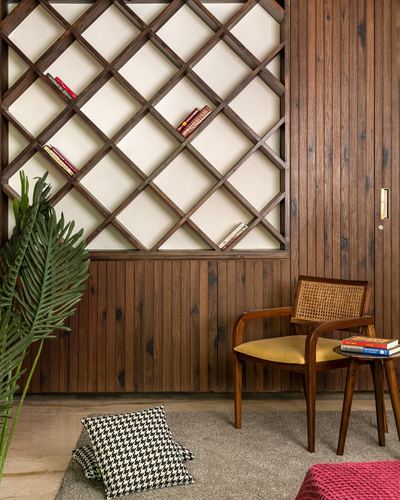 Wood-paneled corner with diagonal lattice bookshelf, cane armchair, and potted palm