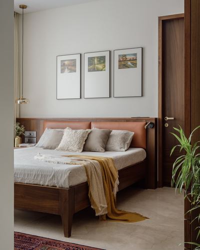 Bedroom with wood bed, leather headboard, triptych art, and open wooden door framing a plant