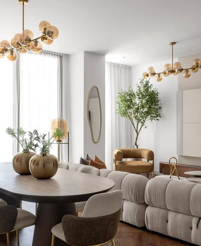 Open living-dining space with round stone table, beige sectional, and bubble chandeliers in warm neutral tones