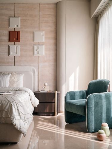 Bedroom with travertine-clad wall, sculptural art panels, and teal velvet curved armchair beside window