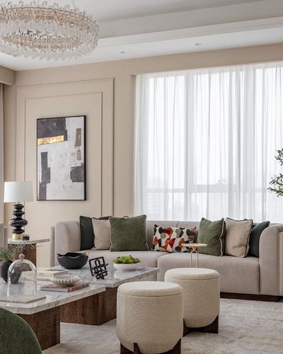Beige living room with sofa, patterned cushions, marble coffee table, ottomans, and crystal chandelier