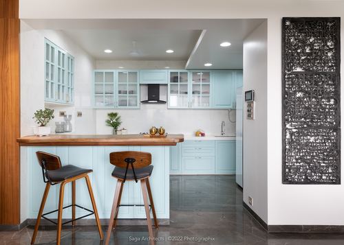 Pastel blue open kitchen with wood-topped breakfast counter and two bar stools, dark carved panel on adjacent wall