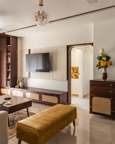 Living room with wood-panelled TV wall, cane sideboard, mustard bench and arched doorway