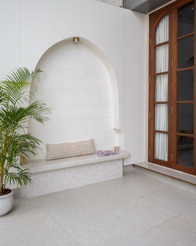 Arched niche with stone bench beside an arched teak glass door and potted palm