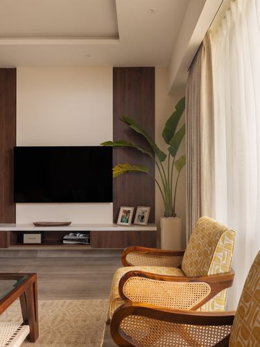 Living room corner with cane armchairs, wood-panelled TV wall, and sheer curtained window