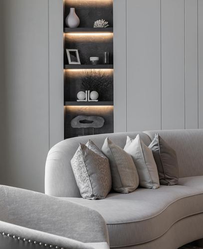 Curved greige sofa with patterned cushions beneath a backlit display niche with decorative objects
