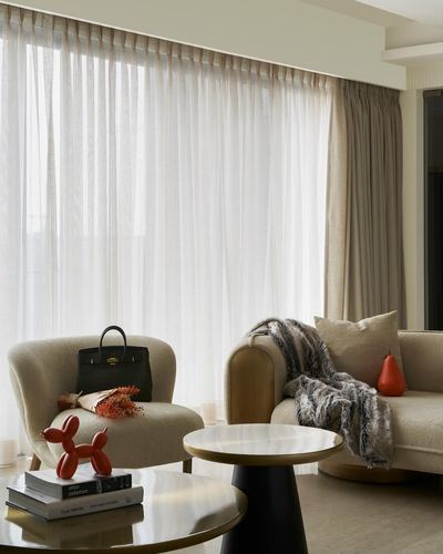 Living room corner with cream armchair, sofa, marble side tables and sheer curtains