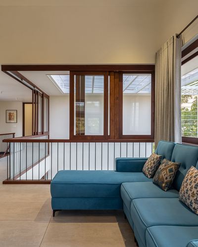 Teal sectional sofa beside a stair railing under a double-height skylight with wooden sliding windows