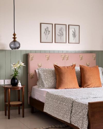 Bedroom with pink floral headboard, green wainscot panelling, and orange velvet cushions on a patterned bedspread