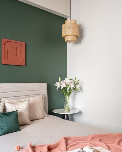 Bedroom corner with green accent wall, cane pendant light, beige headboard and terracotta throw