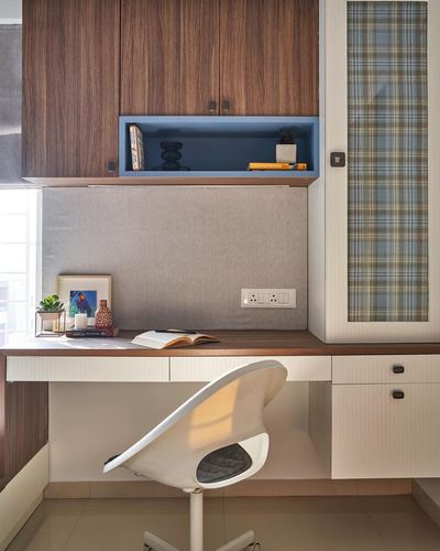 Study nook with wood cabinets, blue display niche, grey upholstered panel and white desk chair