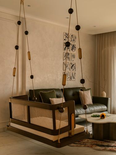 Cane-panelled hanging swing with bead ropes in front of an olive leather sofa and textured plaster wall