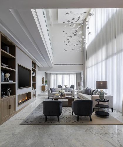 Double-height living room with marble floor, built-in fireplace unit, and floor-to-ceiling sheer curtains