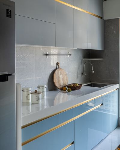 Modern kitchen with blue gloss cabinets, brass trim, marble-look backsplash and white countertop
