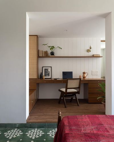 Study nook with wooden desk, cane chair, floating shelf, framed through an archway with patterned green floor tiles