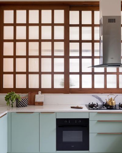 Sage green kitchen with marble-look counter and wood-framed ribbed glass sliding panels behind hob