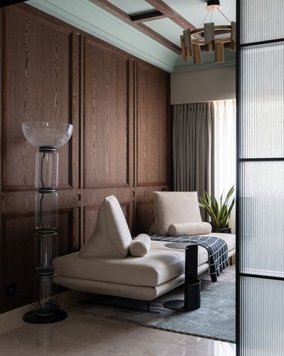 Wood-panelled seating nook with beige daybed, sculptural floor lamp, and reeded glass partition