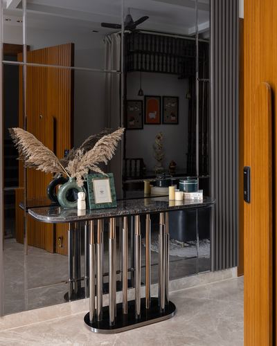 Foyer console table with pampas grass in front of a mirrored wall beside a fluted wooden door