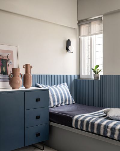 Corner bedroom nook with fluted blue panelling, built-in bed, striped linens, and terracotta vases on a chest of drawers.