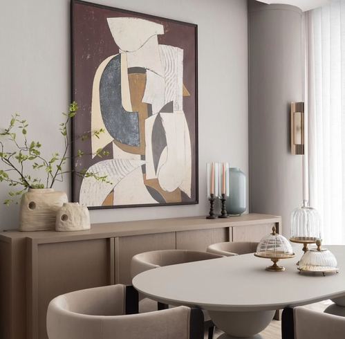 Curved dining table with taupe chairs beneath abstract art above a wood sideboard