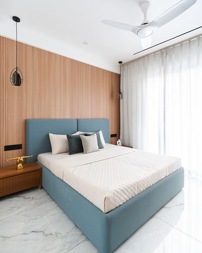 Bedroom with teal upholstered bed against fluted wood wall and marble flooring