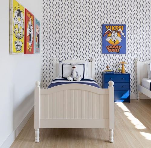 Kids bedroom with two white twin beds, navy patterned wallpaper, and colorful Looney Tunes artwork