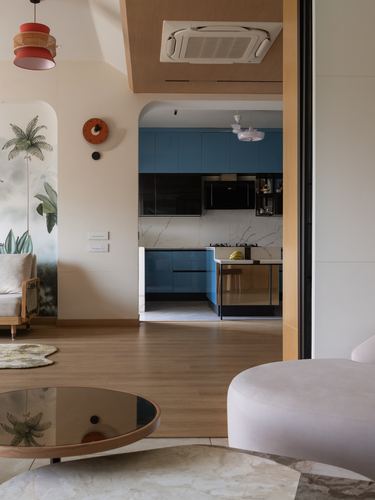 Living room with wood floor and glass table opening through arch to blue kitchen