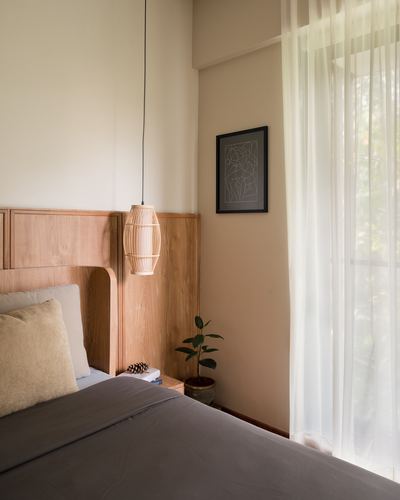 Bedroom corner with curved wood headboard, woven pendant lamp, sheer curtain and framed line art
