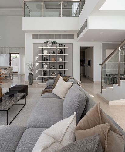 Grey sectional sofa in double-height living room with open shelving and mezzanine above