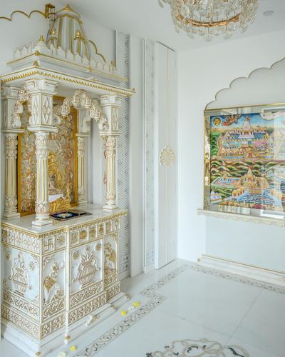 White and gold carved marble mandir beside a framed miniature painting in a Mumbai home