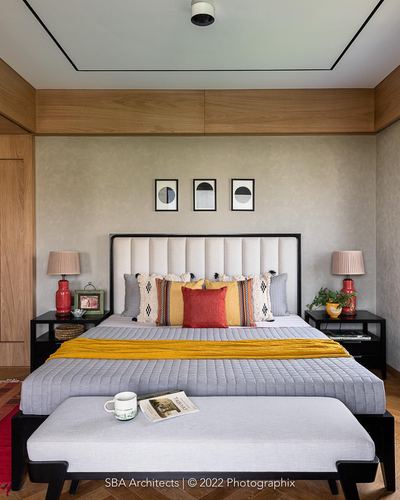 Bedroom with tufted headboard, mustard throw, red lamps and a bench with mug and magazine