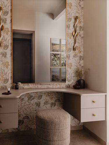 Curved floating dressing table with mirror, floral wallpaper, brass sconces, and boucle ottoman
