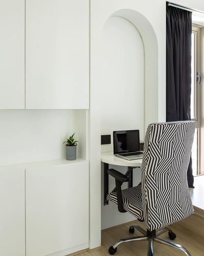 Arched wall niche with fold-down desk, laptop, and striped chair beside built-in white cabinetry