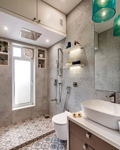 Bathroom with grey stone walls, patterned floor tile, oval vessel sink and teal pendant lights