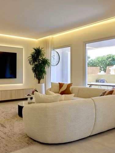 Cream boucle curved sectional in a minimalist living room with cove lighting and glass doors to outdoor terrace